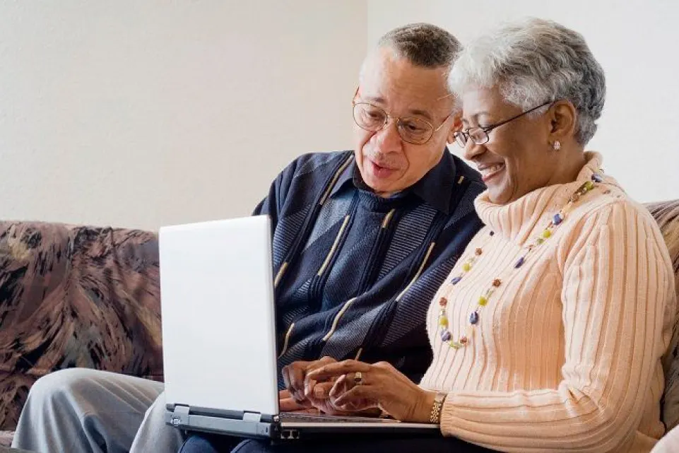 an old man and women look at laptop screen and smile